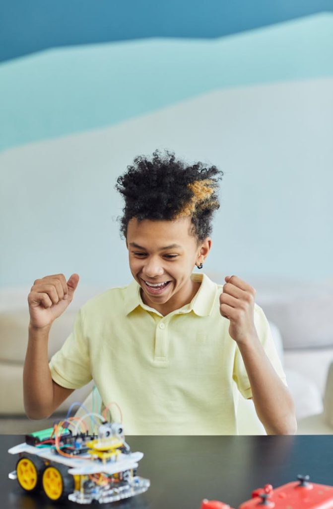 Teen boy enthusiastically works on a robotics project indoors, smiling and engaging.